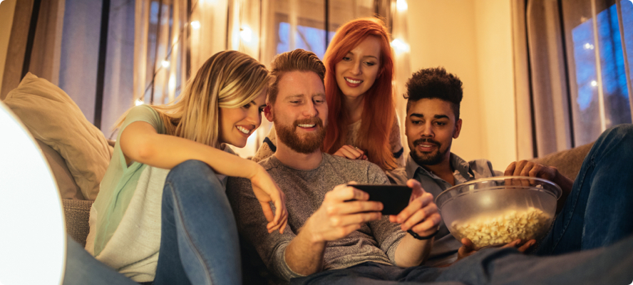 Four people huddled around a smartphone streaming Sling TV