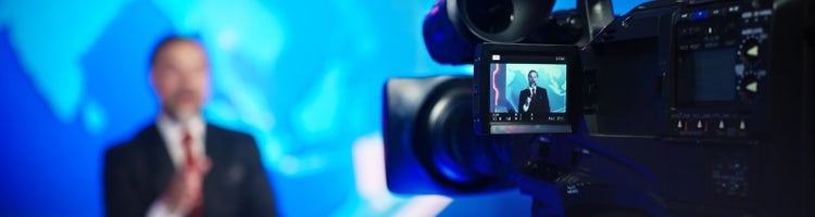 An image of a video camera filming a news anchor.