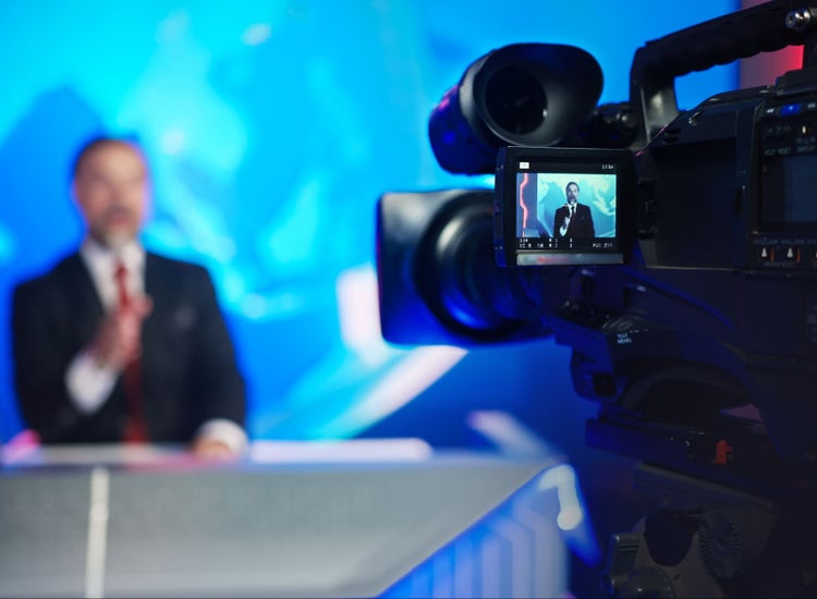An image of a video camera filming a news anchor.